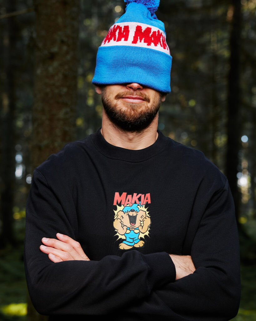 Man standing in forest wearing blue Bamse Makia hat and a black sweater